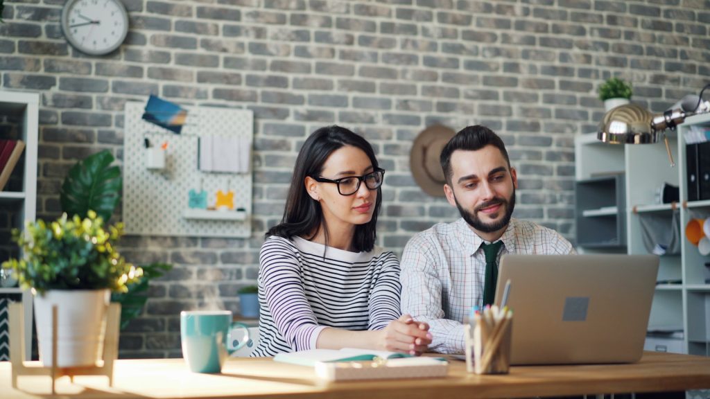 a man and woman sitting at a table looking at a laptop